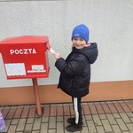 dziewczynka ubrana w czarną kurtkę i niebieską czapke wrzuca kartkę pocztowa do skrzynki pocztowej.jpg