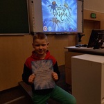 Chłopiec trzyma dyplom na tle tablicy multimedialnej z prezentacją.jpg